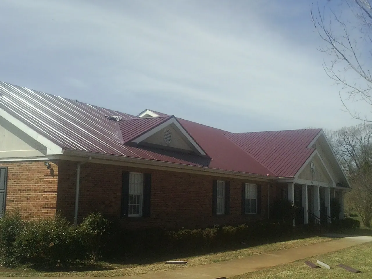 Red metal roof with gabled entries on a long brick building, from a Hail Damage Roof Repair job in Monroe Bridge