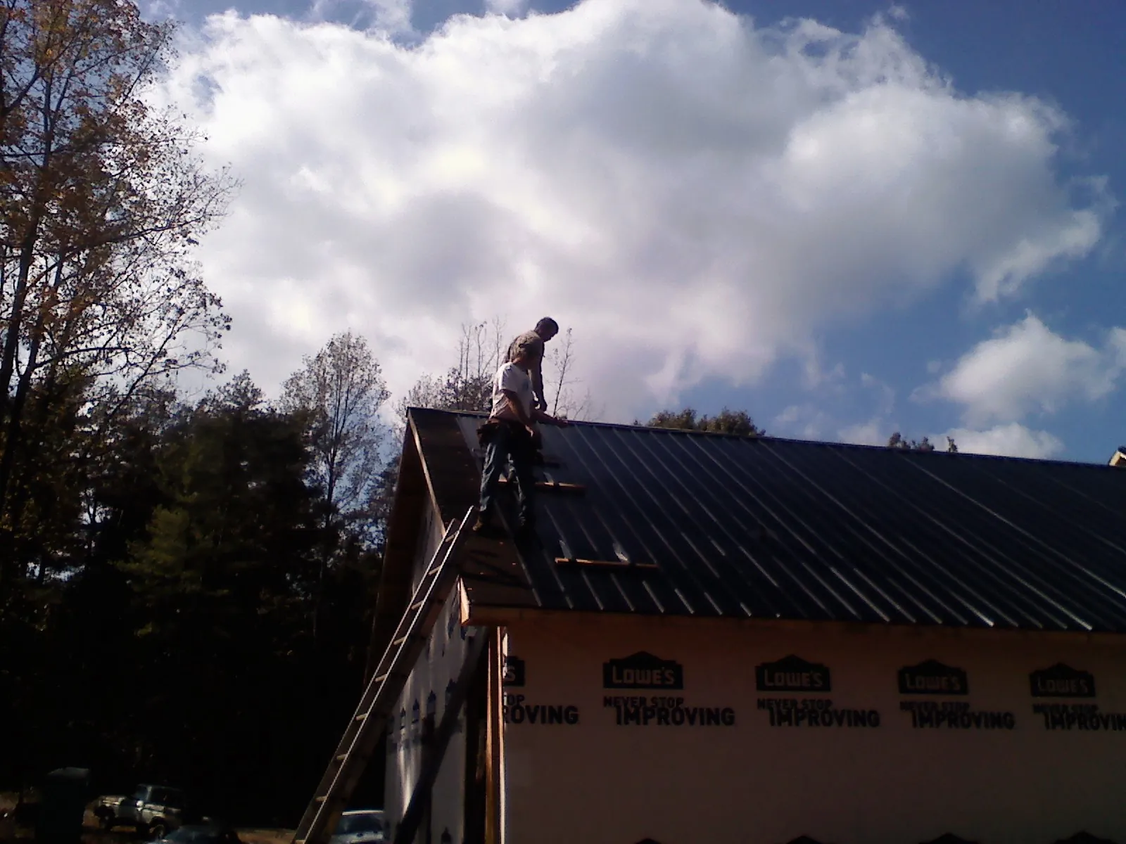 Roofer fastening dark metal panels high against a cloudy sky, from a Roof Inspection job in Monroe Bridge